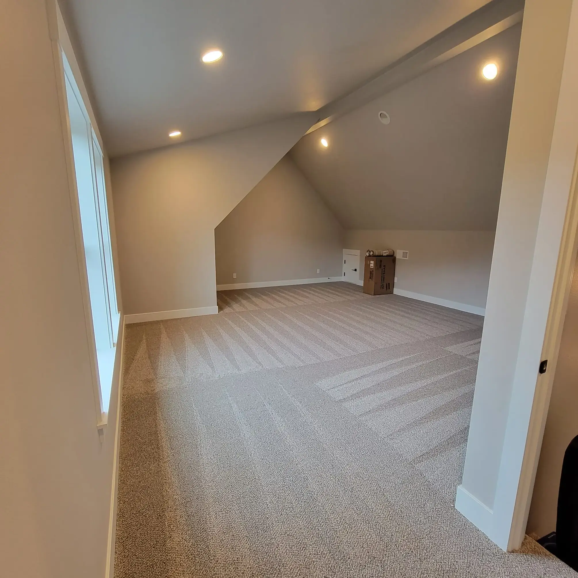 Spacious attic with sloped ceiling and carpeted floor.
