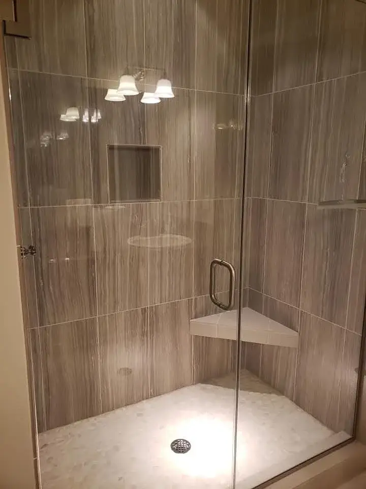 Modern glass shower with corner shelf and lighting.